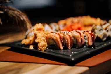 Konforlu bir restoranda çeşitli rulo ve kızarmış elementlerin yer aldığı lezzetli suşi tabağı.