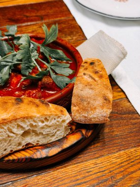 Sıcak yemek ortamında, ahşap sofrada servis edilen taze ekmek ve sağlıklı güveç.