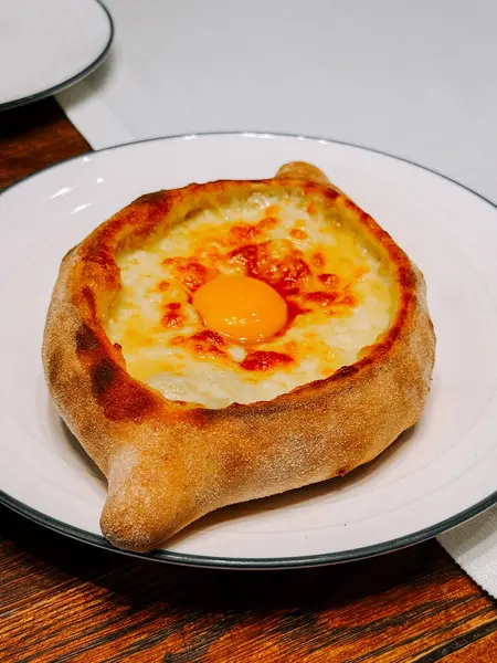 Lezzetli Khachapuri, sıcak bir yemek ortamında beyaz bir tabakta servis edilir.