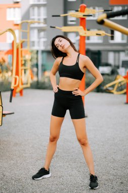 Kadın şehir ortamında spor yaparken spor salonunda esneme hareketleri yapıyor.