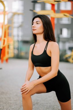 Genç bir kadın gündüz antrenmanı sırasında açık hava fitness parkında hamle yapıyor.