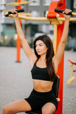 Spor meraklısı yaz boyunca şehir parkındaki spor salonunda üst vücut egzersizi yapıyor.