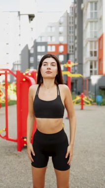 Genç bir kadın şehir parkında spor yapıyor. Siyah spor kıyafetleri giyiyor ve spor kıyafetlerini sergiliyor.