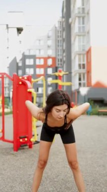 Genç kadın şehir parkında spor yapıyor. Açık hava spor aletleri kullanıyor.