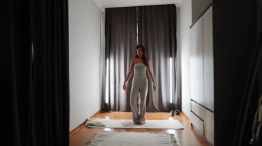 Zarif kıyafetli bir kadın minimalist bir dekorla aydınlık bir odada yürür.