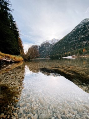Şafak vakti sakin sulara yansıyan görkemli dağlar huzurlu doğal bir manzarada.
