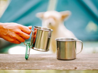 Açık hava macerası sırasında bir köpek yakınlarda beklerken, bir kamp kupasını tutan el.
