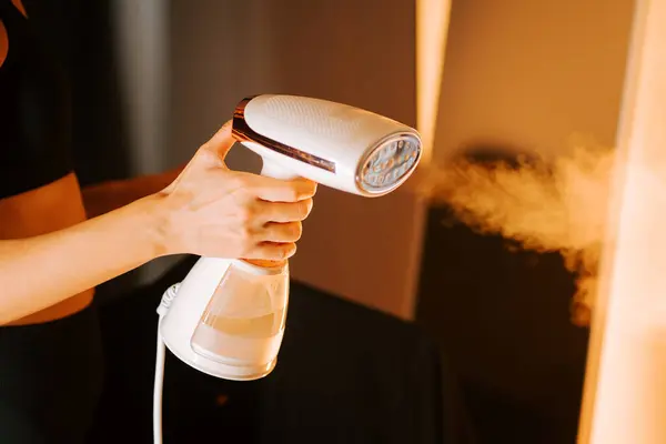 İç mekan ortamında gömleğindeki kırışıklıkları silmek için buharlı kıyafet kullanan kadın.