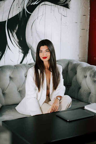 Stylish woman in a white suit relaxes on a tufted couch in a modern interior setting