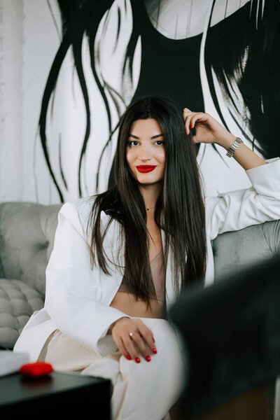 Model in stylish white outfit poses confidently on sofa with artistic backdrop