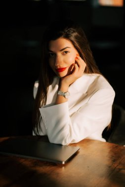 Zarif kadın, rahat ve loş bir çalışma alanındaki masada düşünceli bir şekilde poz veriyor.