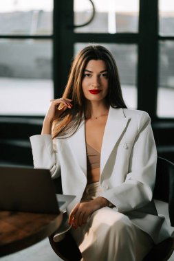 Modern ofis ortamındaki iş kadını arka planda dizüstü bilgisayarla rahatça poz veriyor