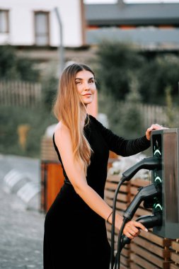 Genç bir kadın güneşli bir öğleden sonra şehir merkezinde elektrikli araç yüklüyor.