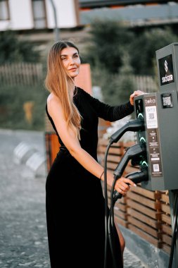 Açık havada elektrikli araba şarj aleti kullanan zarif bir kadın.