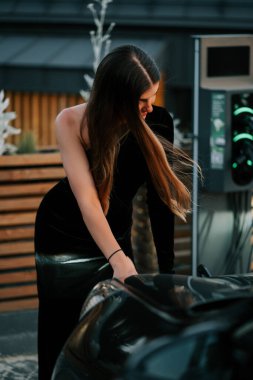 Şık bir kadın, şehir şarj istasyonunda lüks arabalarla etkileşime giriyor.