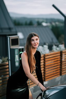 Model, alacakaranlıkta şık bir arabanın yanında çarpıcı bir manzarayla şık bir poz veriyor.