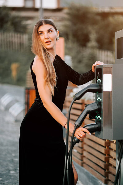 Молодая женщина заряжает электромобиль на зарядной станции в городской обстановке во второй половине дня