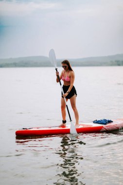 Kadınlar güneşli bir öğleden sonra sakin bir gölde ayakta sörf yapmayı severler.
