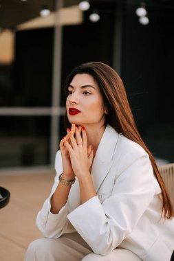 Zarif giyinmiş bir kadın düşünceli bir şekilde akşam ışığında dışarıda poz veriyor.