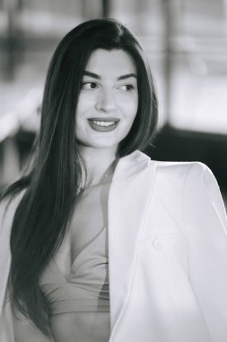 Şık giyinmiş zarif bir kadın, şehir meydanında akşam etkinliğinde gülümsüyor.