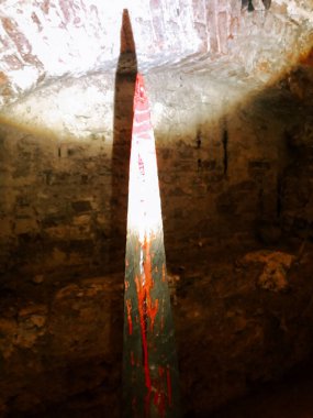 Tall wooden structure casts a sharp shadow in a dimly lit underground space