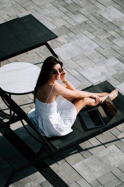 Genç bir kadın güneşli bir günde havuzda dinleniyor. Beyaz bir elbise içinde.