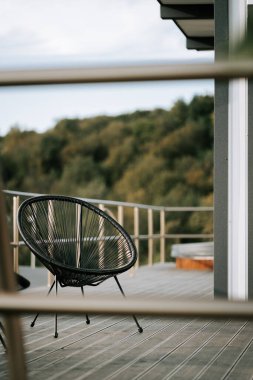 Gündüz vakti yemyeşil manzaraya bakan balkondaki modern açık hava koltuğu.