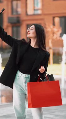 Şık bir kadın güneşli bir günde şehir merkezinde alışveriş yaparken selfie çeker.