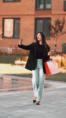 Genç bir kadın güneşli öğleden sonra şehir parkında parlak bir çantayla alışveriş yapıyor.