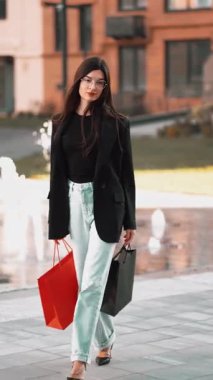 Genç bir kadın modern bir çeşme alanının yanında şık bir kıyafetle alışveriş yapmaktan hoşlanıyor.