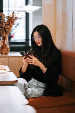 Genç bir kadın, öğle saatlerinde rahat bir kafede akıllı telefon kullanıyor.