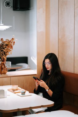 Dekoratif çiçekler ve atıştırmalıklarla dolu rahat bir kafede akıllı telefon kullanan bir kadın.