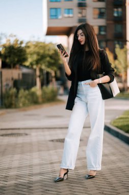 Stylish young woman checking her phone while standing in an urban setting during the day
