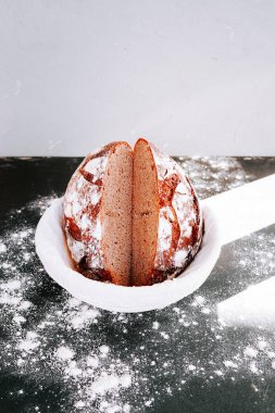 Freshly baked round bread with a clean cut placed on a surface dusted with flour