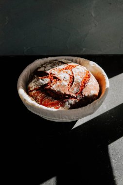 Karanlık bir yüzeyde, bir kâsede taze pişmiş ekmek ve doğal ışık.