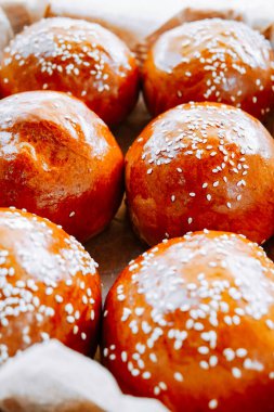 Sıcak bir mutfak ortamında susam tohumlarıyla kaplı taze pişmiş ekmek ruloları.