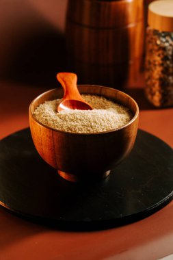 Tahta bir kasede kuskus, yanında kaşıkla karanlık bir masanın üstünde konteynırlar.