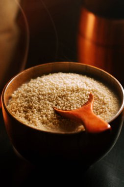 Ahşap bir kasede pişmemiş kuskus ve bir kepçe yemek.