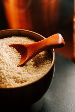 Pişmemiş kuskus ahşap bir kasede servis edilir ve sıcak bir mutfak ortamında kullanıma hazır bir kepçe ile.