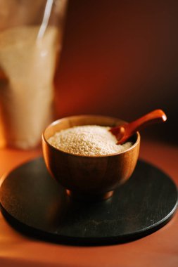 Sıcak ışıklandırmalı, siyah bir yüzeyde, ahşap bir kasede pişmemiş kuskus keşfedin.