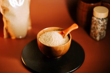 Tahta bir kasede kuskus, koyu bir yüzeye sergilenmiş bir kaşıkla. İçindekilerle çevrili.