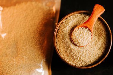 Ahşap bir kasede pişmemiş kuskus ve siyah bir mutfak yüzeyi keşfedin.