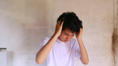 Yakışıklı Asyalı adam iki eliyle başını tutuyor. Baş ağrısı