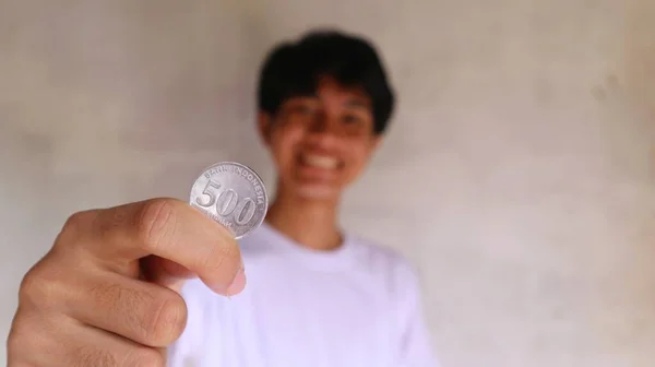 白いTシャツのアジア人男性がインドネシアのコインを保持し 示しています — ストック写真