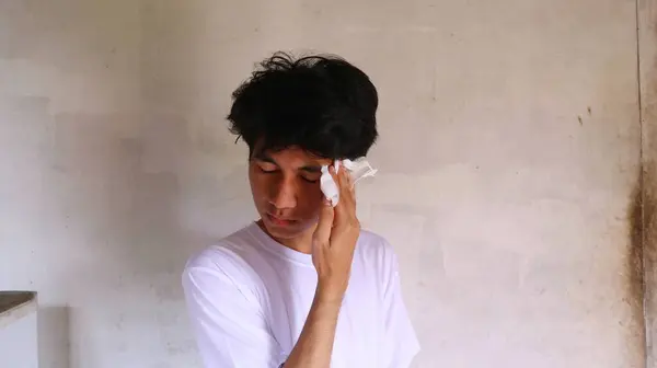 白いTシャツのアジア人男性がティッシュで顔を拭いています — ストック写真