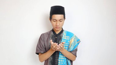 Asyalı Müslüman bir adam iki eliyle beyaz bir arka planda dua ediyor.