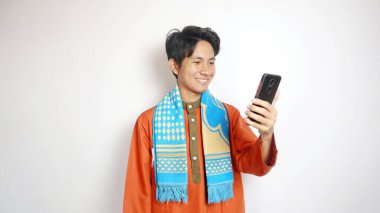 Heyecanlı Asyalı Müslüman adam elinde beyaz bir arka planda akıllı telefon tutuyor.