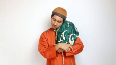 Asyalı Müslüman adam beyaz arka planda destek yastığına sarılmış el kol hareketi yapıyor.