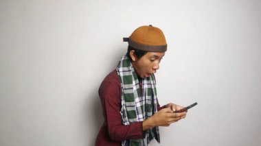Şok olmuş Asyalı Müslüman adam oynuyor, beyaz arka planda akıllı telefondan yazı yazıyor.