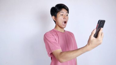 Asyalı bir adam beyaz arka planda jest yaparak ve akıllı telefon tutarak şoka girdi.